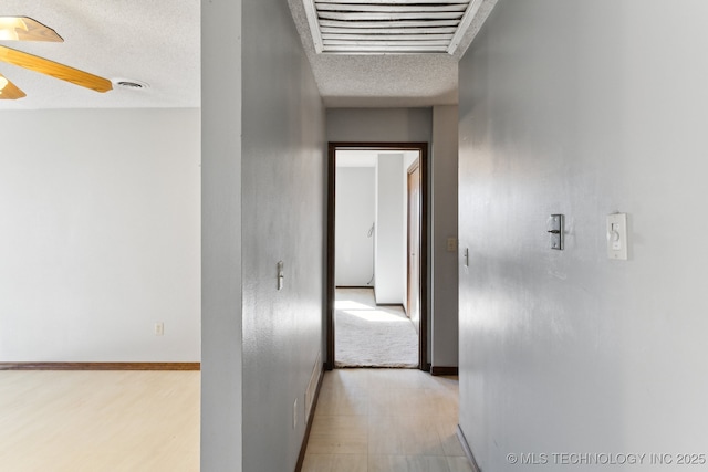 hall featuring visible vents, baseboards, a textured ceiling, and light floors