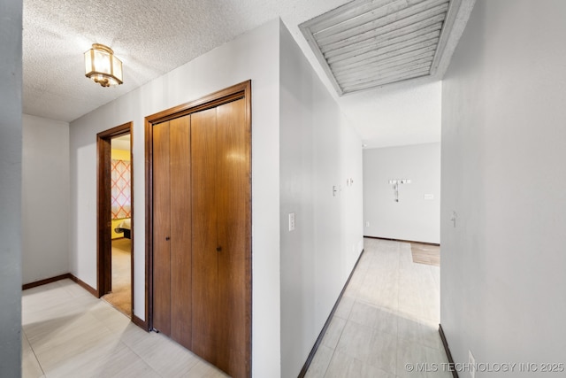 hall featuring light floors, a textured ceiling, and baseboards