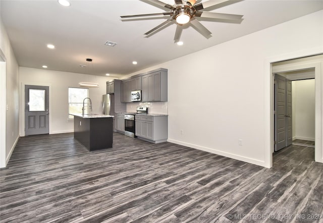 kitchen with pendant lighting, dark hardwood / wood-style flooring, stainless steel appliances, gray cabinets, and a center island with sink