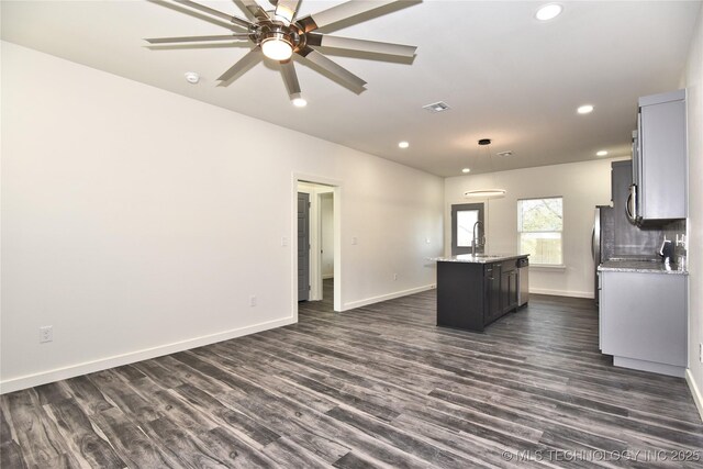 kitchen with a kitchen island with sink, dark wood-type flooring, pendant lighting, light stone counters, and sink