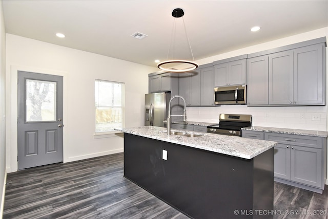 kitchen featuring an island with sink, stainless steel appliances, gray cabinetry, pendant lighting, and sink