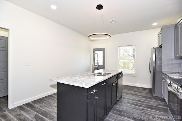 kitchen with sink, appliances with stainless steel finishes, a kitchen island with sink, light stone countertops, and decorative light fixtures