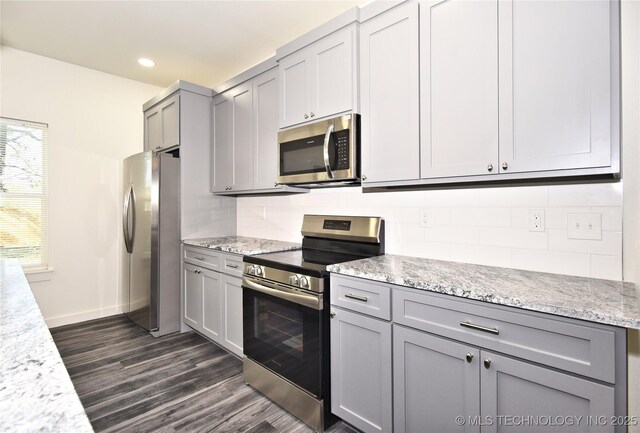 kitchen with dark hardwood / wood-style floors, gray cabinets, decorative backsplash, light stone countertops, and stainless steel appliances