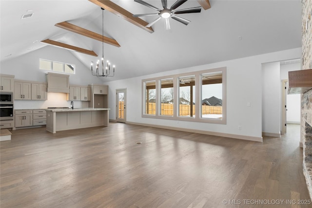 unfurnished living room with beam ceiling, wood finished floors, high vaulted ceiling, baseboards, and ceiling fan with notable chandelier