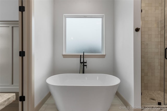 bathroom with a freestanding tub, a shower stall, and baseboards