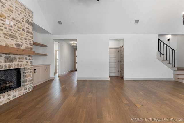 unfurnished living room featuring a fireplace, visible vents, vaulted ceiling, stairway, and dark wood-style floors