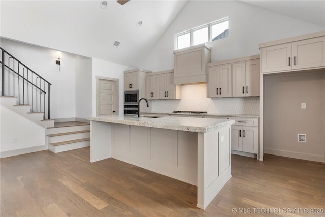 kitchen featuring an island with sink, light wood finished floors, visible vents, and a sink