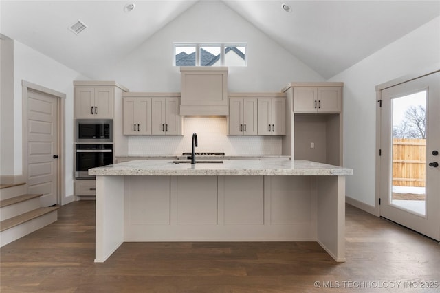 kitchen featuring built in microwave, visible vents, a kitchen island with sink, and stainless steel oven