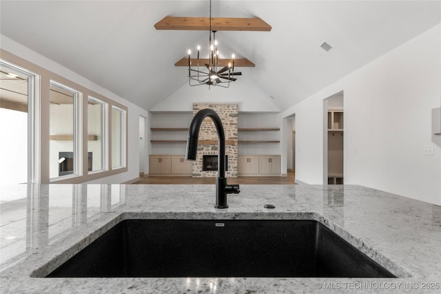 kitchen featuring decorative light fixtures, a fireplace, open floor plan, a sink, and light stone countertops