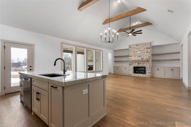 kitchen featuring a fireplace, a sink, open floor plan, light stone countertops, and an island with sink