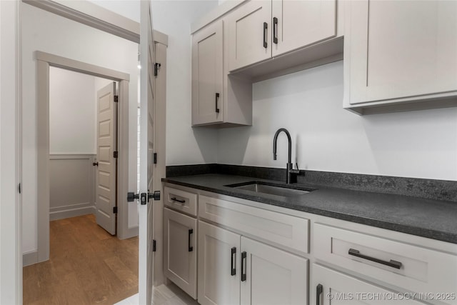 kitchen featuring dark countertops, white cabinets, a sink, and light wood-style flooring