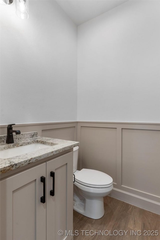 bathroom with a wainscoted wall, wood finished floors, vanity, and toilet