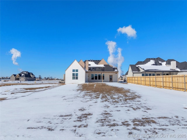 snow covered house featuring a residential view and fence