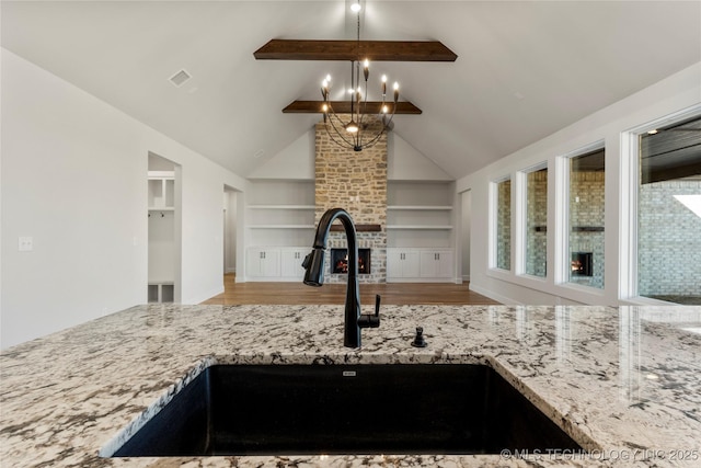 kitchen featuring built in shelves, sink, light stone counters, decorative light fixtures, and beamed ceiling