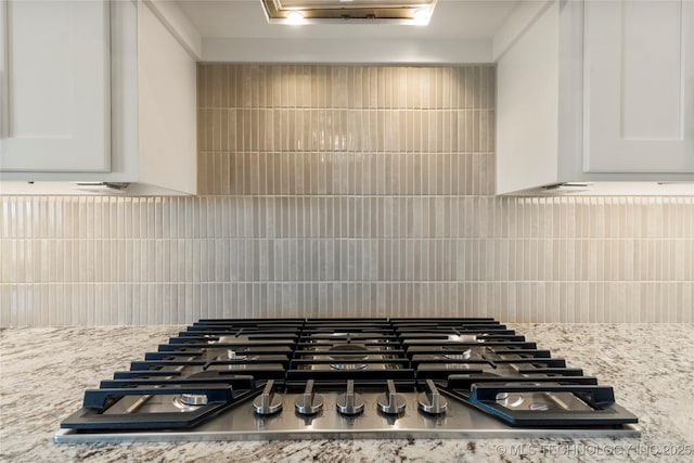 interior details featuring stainless steel gas stovetop, white cabinets, light stone counters, and decorative backsplash