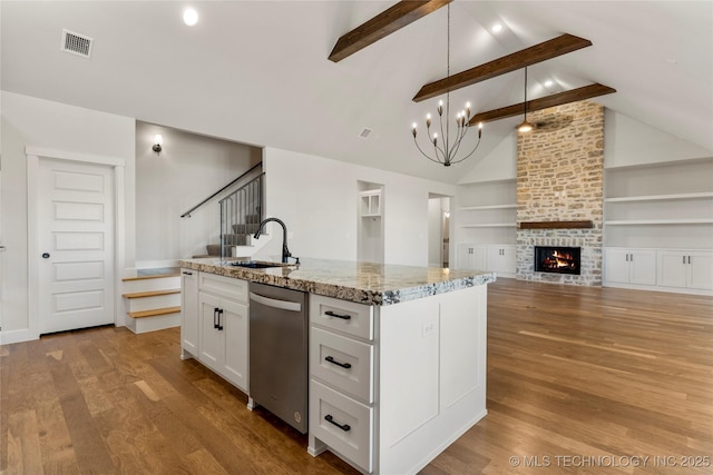 kitchen featuring light stone counters, stainless steel dishwasher, an island with sink, pendant lighting, and white cabinets