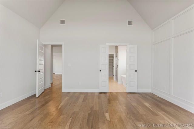 unfurnished bedroom featuring high vaulted ceiling and light hardwood / wood-style floors