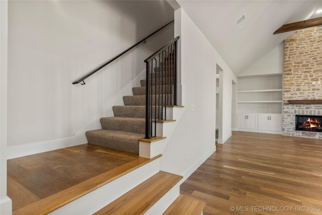 staircase featuring wood-type flooring, high vaulted ceiling, a brick fireplace, built in features, and beamed ceiling