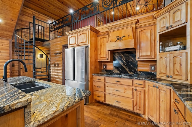 kitchen with sink, appliances with stainless steel finishes, dark stone counters, log walls, and hardwood / wood-style floors