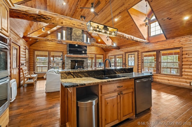 kitchen with sink, ceiling fan, a kitchen island with sink, log walls, and stainless steel dishwasher