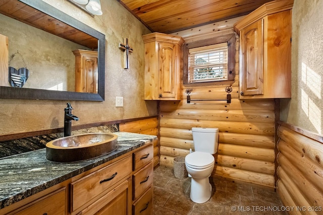 bathroom featuring vanity, wooden ceiling, toilet, and rustic walls