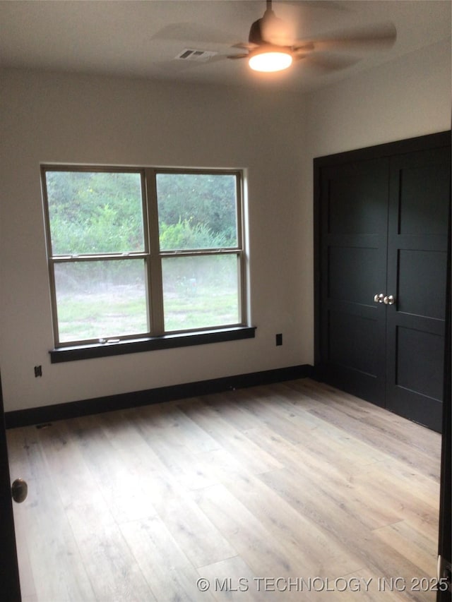 unfurnished bedroom with ceiling fan, light wood-type flooring, a closet, and multiple windows