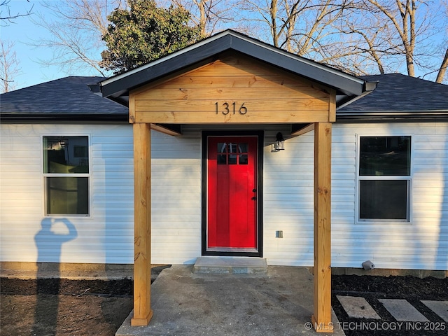 view of exterior entry featuring roof with shingles