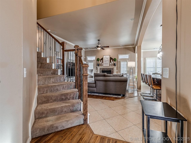 living room with light wood-type flooring, ceiling fan, crown molding, and a brick fireplace