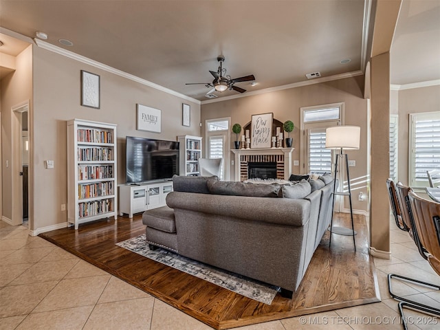 living room with a brick fireplace, a wealth of natural light, light tile patterned floors, and ceiling fan