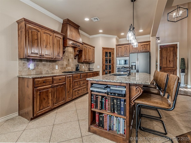 kitchen featuring decorative light fixtures, decorative backsplash, a kitchen island with sink, stainless steel appliances, and light stone counters