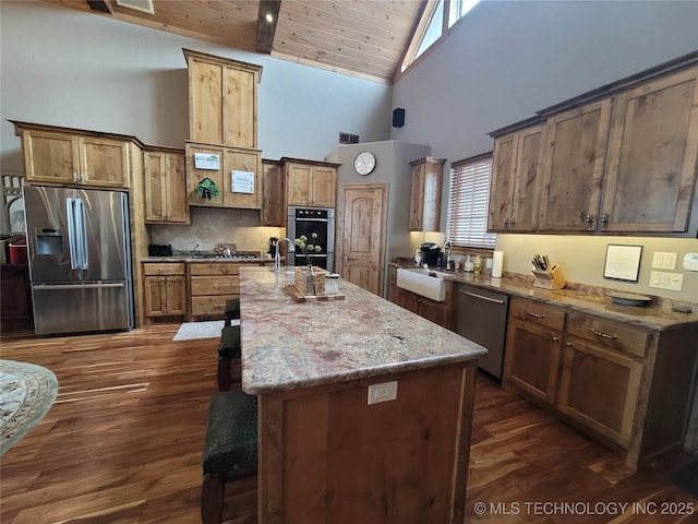 kitchen featuring a center island with sink, sink, appliances with stainless steel finishes, high vaulted ceiling, and light stone counters