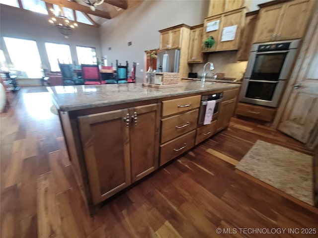 kitchen with stainless steel double oven, dark hardwood / wood-style flooring, an island with sink, sink, and high vaulted ceiling