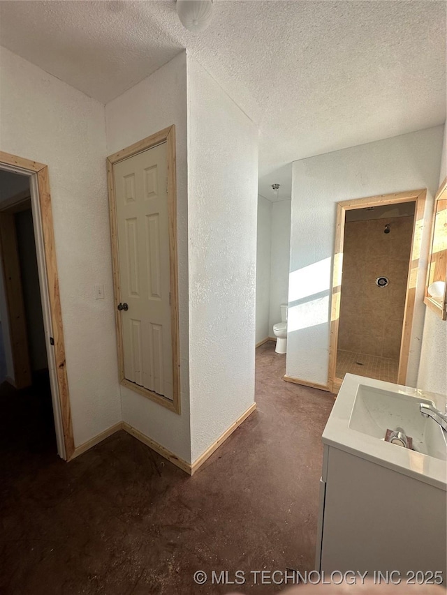 bathroom with toilet, vanity, a shower, a textured ceiling, and concrete flooring