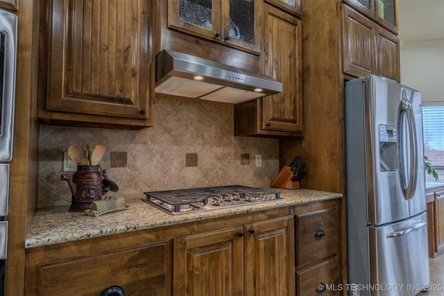 kitchen featuring light stone counters, backsplash, stainless steel appliances, and extractor fan