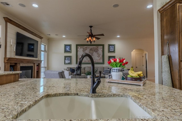 kitchen with ceiling fan, crown molding, sink, and light stone counters