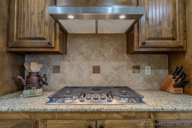 kitchen featuring tasteful backsplash, light stone countertops, stainless steel gas cooktop, and range hood