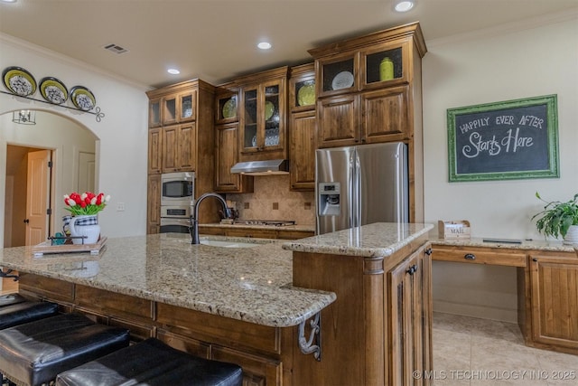 kitchen with an island with sink, stainless steel appliances, crown molding, a breakfast bar, and sink