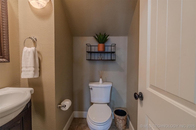 bathroom with toilet, vanity, and lofted ceiling