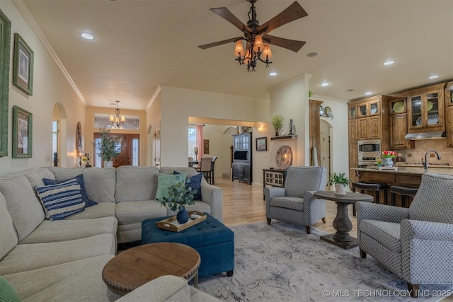 living room with ceiling fan with notable chandelier, light hardwood / wood-style flooring, and crown molding