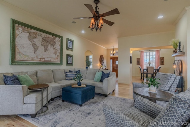 living room with light wood-type flooring, ceiling fan with notable chandelier, and crown molding