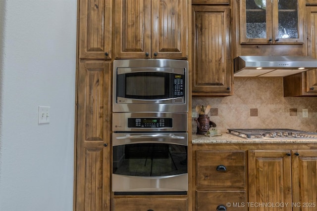 kitchen featuring decorative backsplash, light stone countertops, extractor fan, and stainless steel appliances