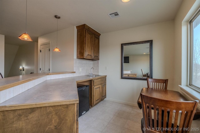 kitchen featuring kitchen peninsula, tasteful backsplash, decorative light fixtures, refrigerator, and sink