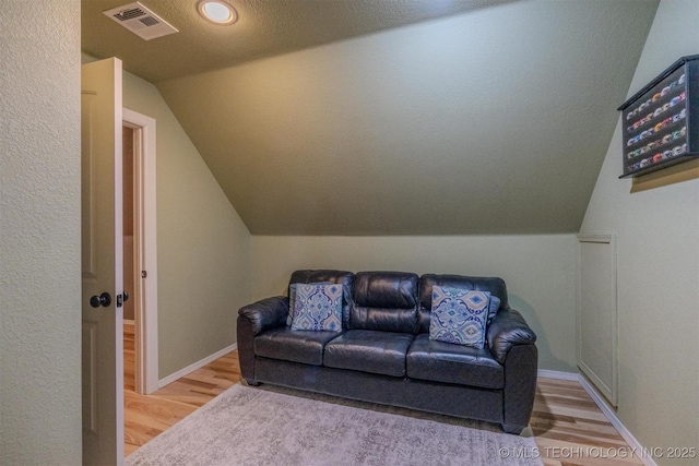 living room with wood-type flooring, a textured ceiling, and vaulted ceiling