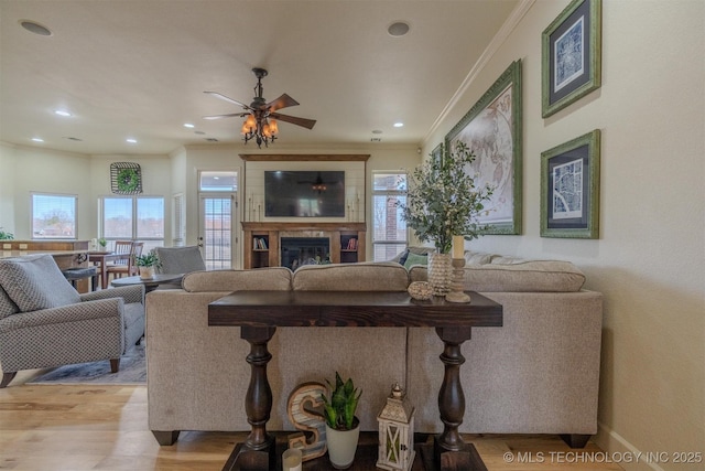 living room featuring light wood-type flooring, ceiling fan, ornamental molding, and a tiled fireplace