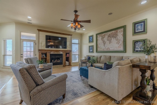 living room featuring light hardwood / wood-style floors, a large fireplace, crown molding, and ceiling fan