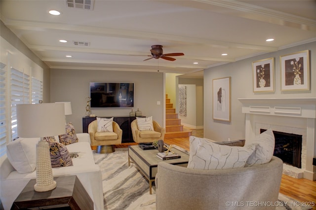 living room featuring ceiling fan, beamed ceiling, crown molding, light hardwood / wood-style flooring, and a high end fireplace