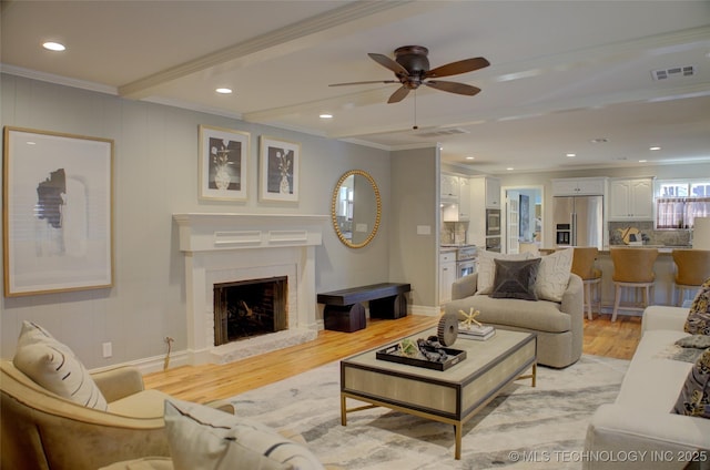 living room featuring ceiling fan, ornamental molding, light hardwood / wood-style floors, and beamed ceiling