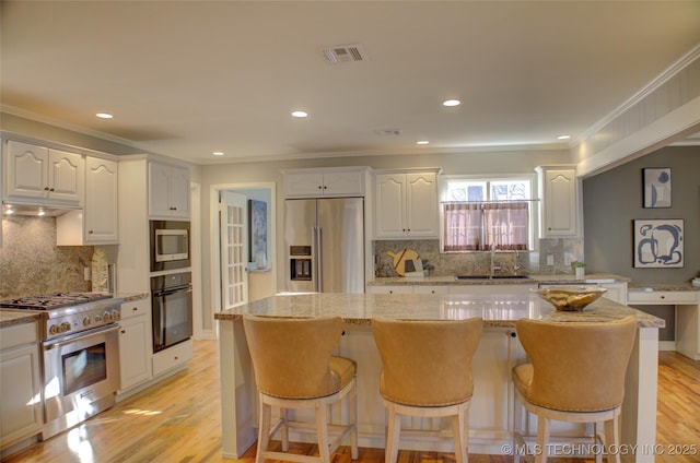 kitchen featuring white cabinetry, a center island, high end appliances, light stone counters, and sink