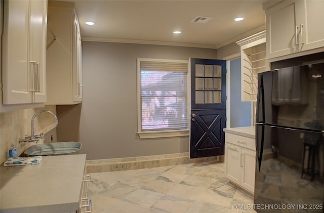 kitchen with white cabinetry, black fridge, crown molding, and a healthy amount of sunlight