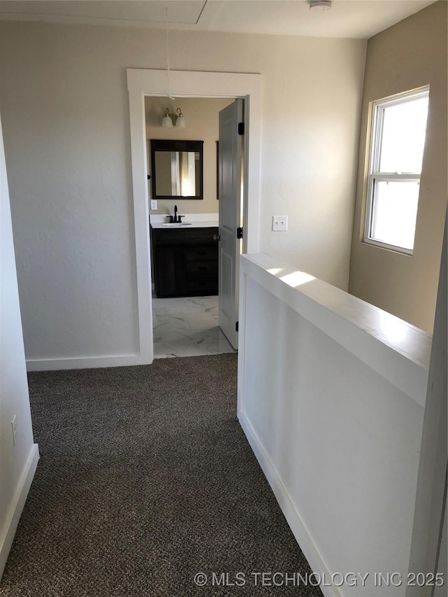 hallway with attic access, carpet flooring, a sink, and baseboards